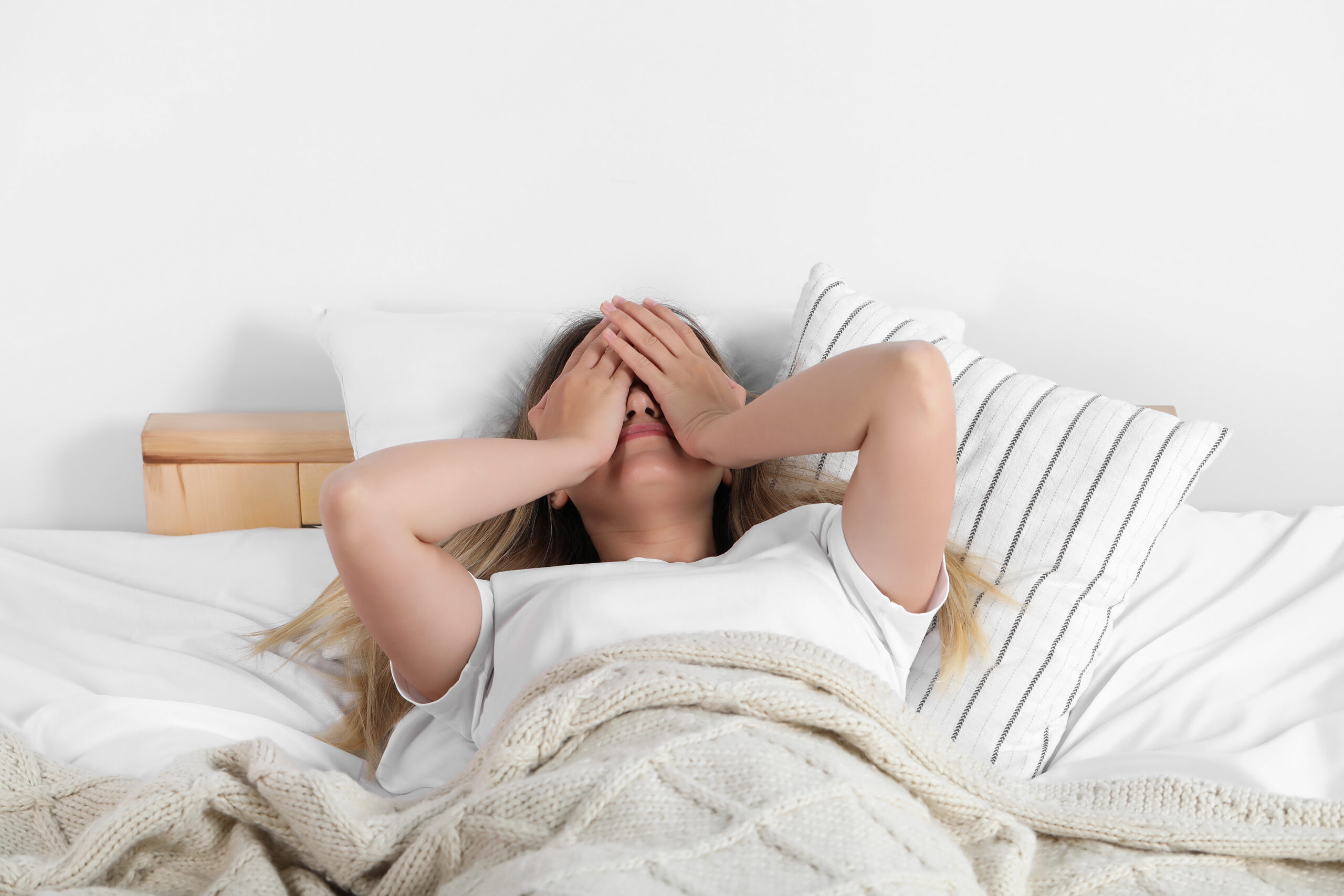 Woman laying in bed with her hands covering her face due to morning sickness symptoms